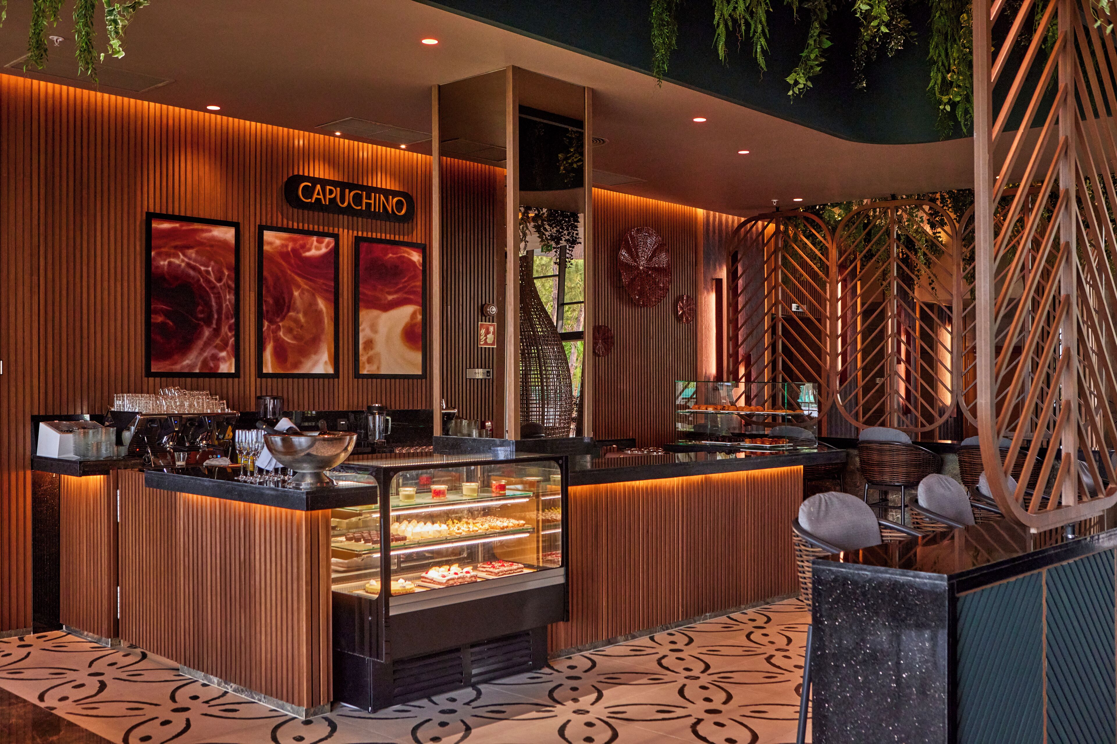 Un restaurant moderne avec un décor intérieur en bois, une vitrine réfrigérée où sont exposés les plats, et une enseigne sur laquelle on peut lire « CAPUCHINO ».