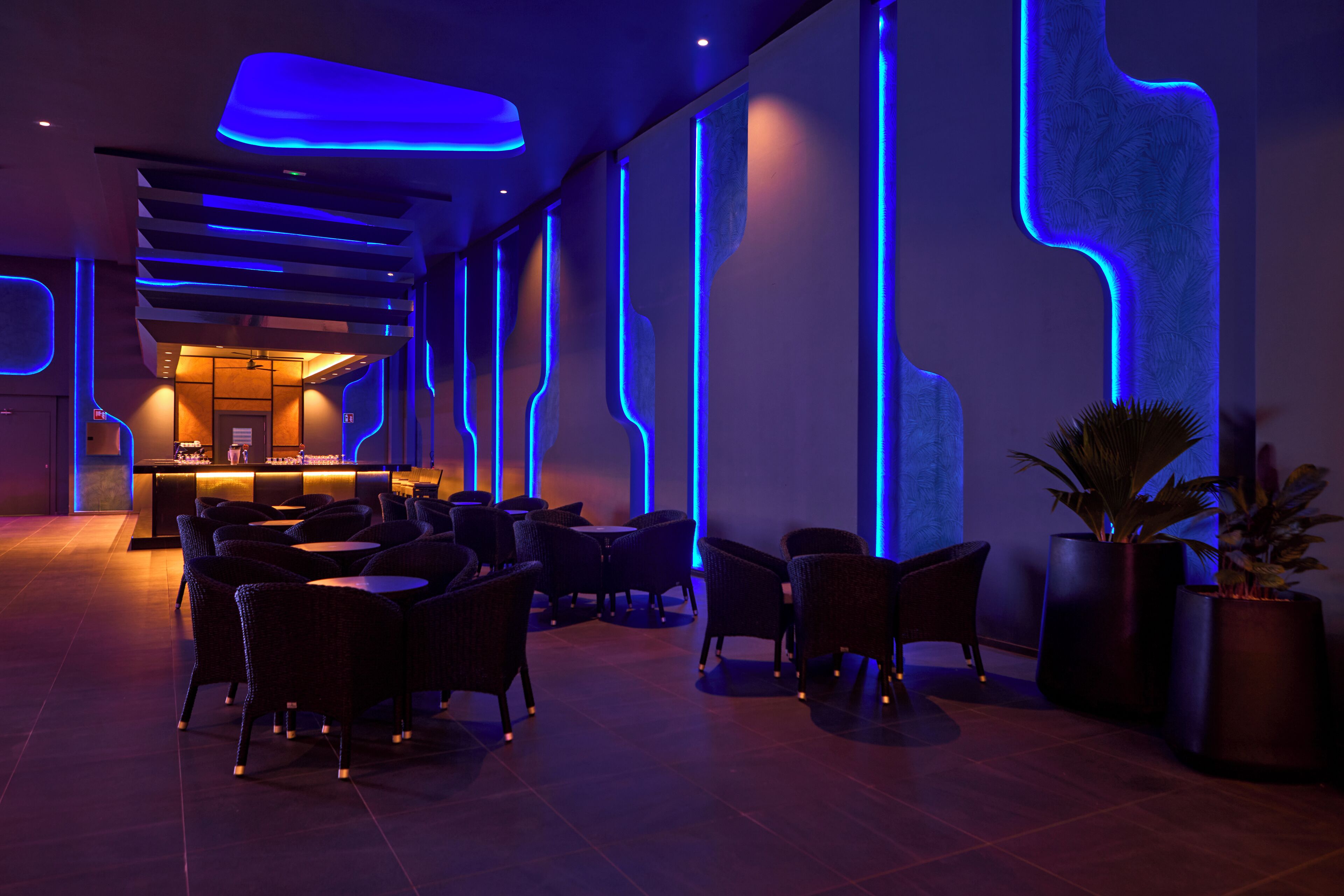 A modern lounge area with seating and a bar, featuring geometric wall designs and ambient lighting.