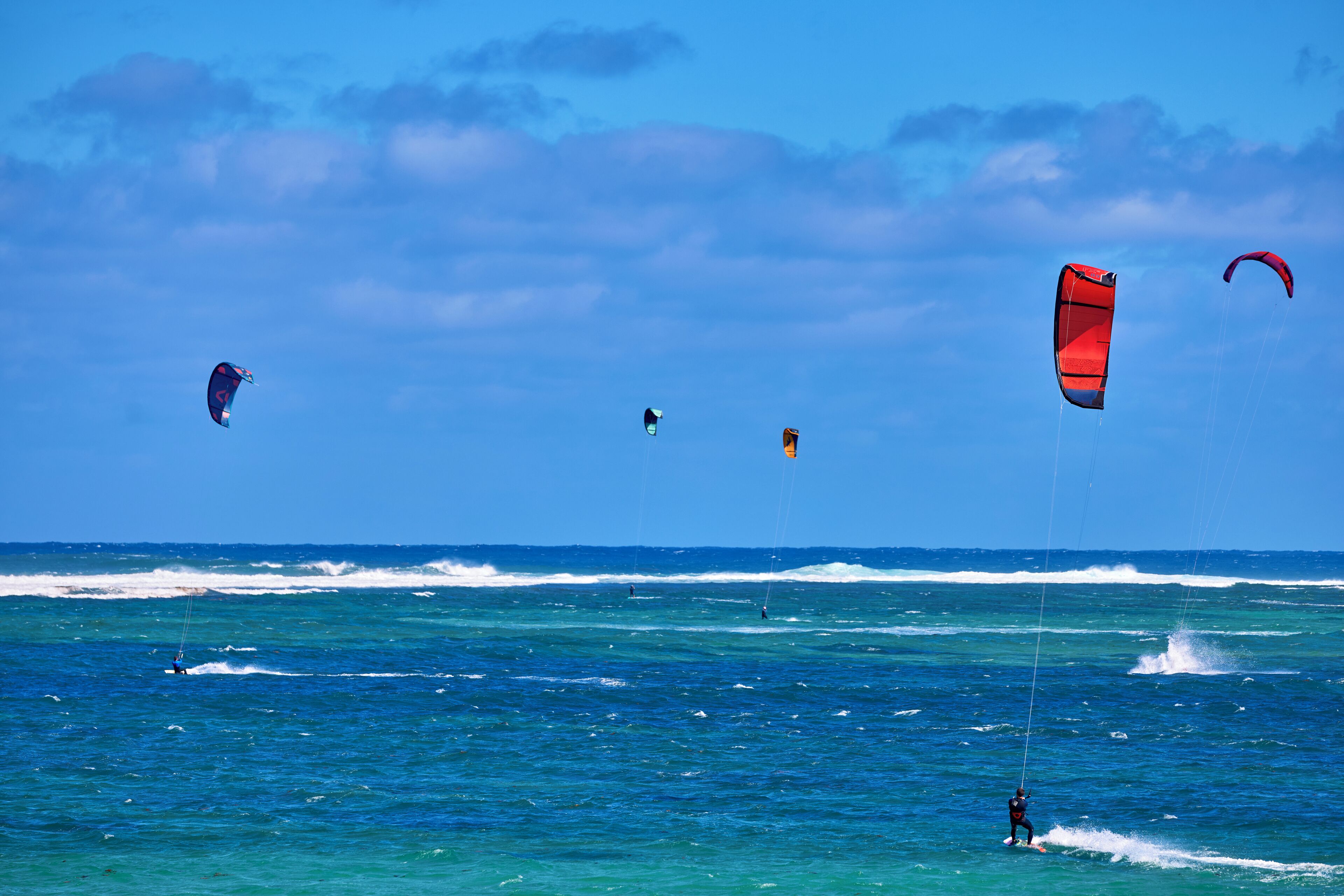 Una playa con agua azul cristalina y algunas personas practicando windsurf.