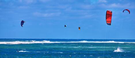 Una playa con agua azul cristalina y algunas personas practicando windsurf.