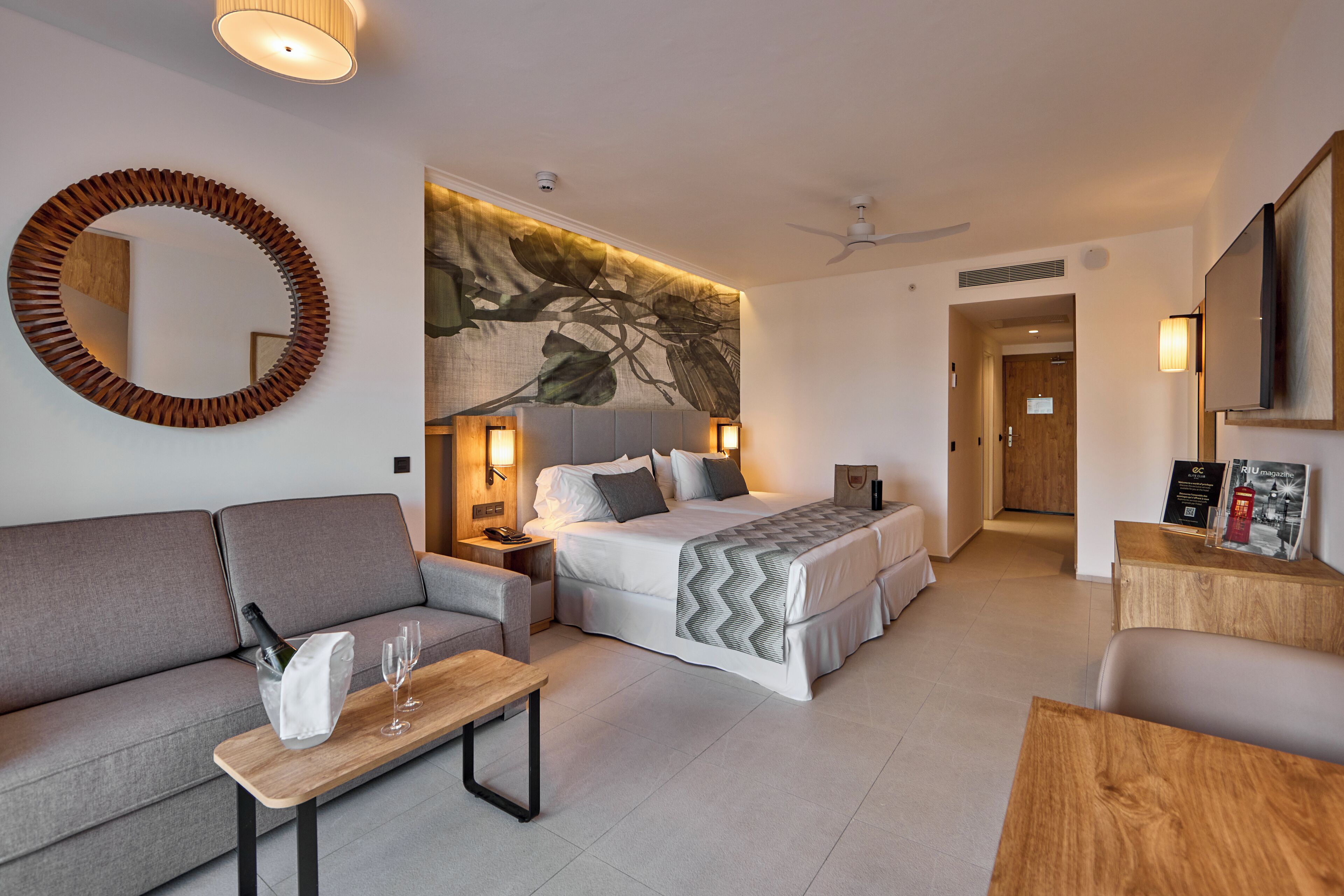 A modern hotel room with a bed, sofa, and a dining table.