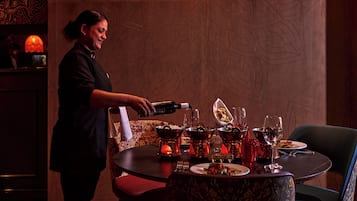 A bar area with a bartender pouring drinks, a table set with plates, glasses, and a bottle.