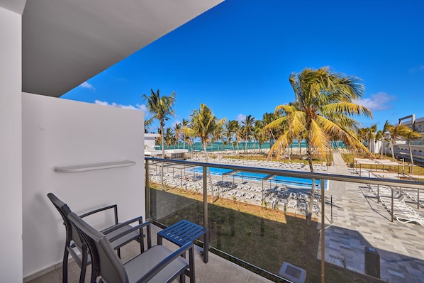 Un balcón con vistas a una zona de piscina, que incluye sillas de descanso y palmeras.