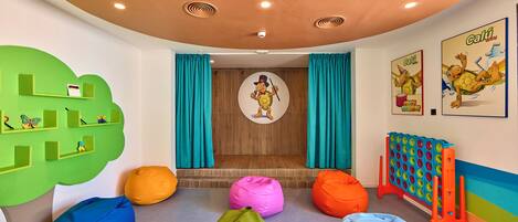 A children's playroom with colorful bean bags, a green tree-shaped shelf, and a turtle-themed wall decoration.