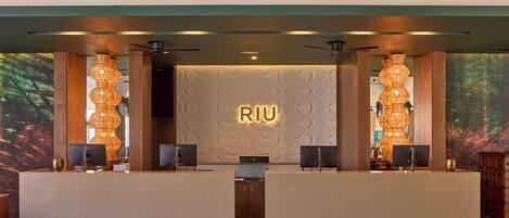 A reception area with a modern design, featuring a reception desk, two large wall-mounted speakers, and a large illuminated sign.