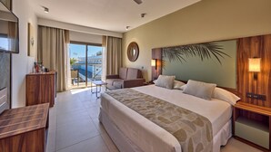 Habitación de hotel con una cama grande, un escritorio, una silla, una mesita y un ventilador de techo, con vista al exterior.