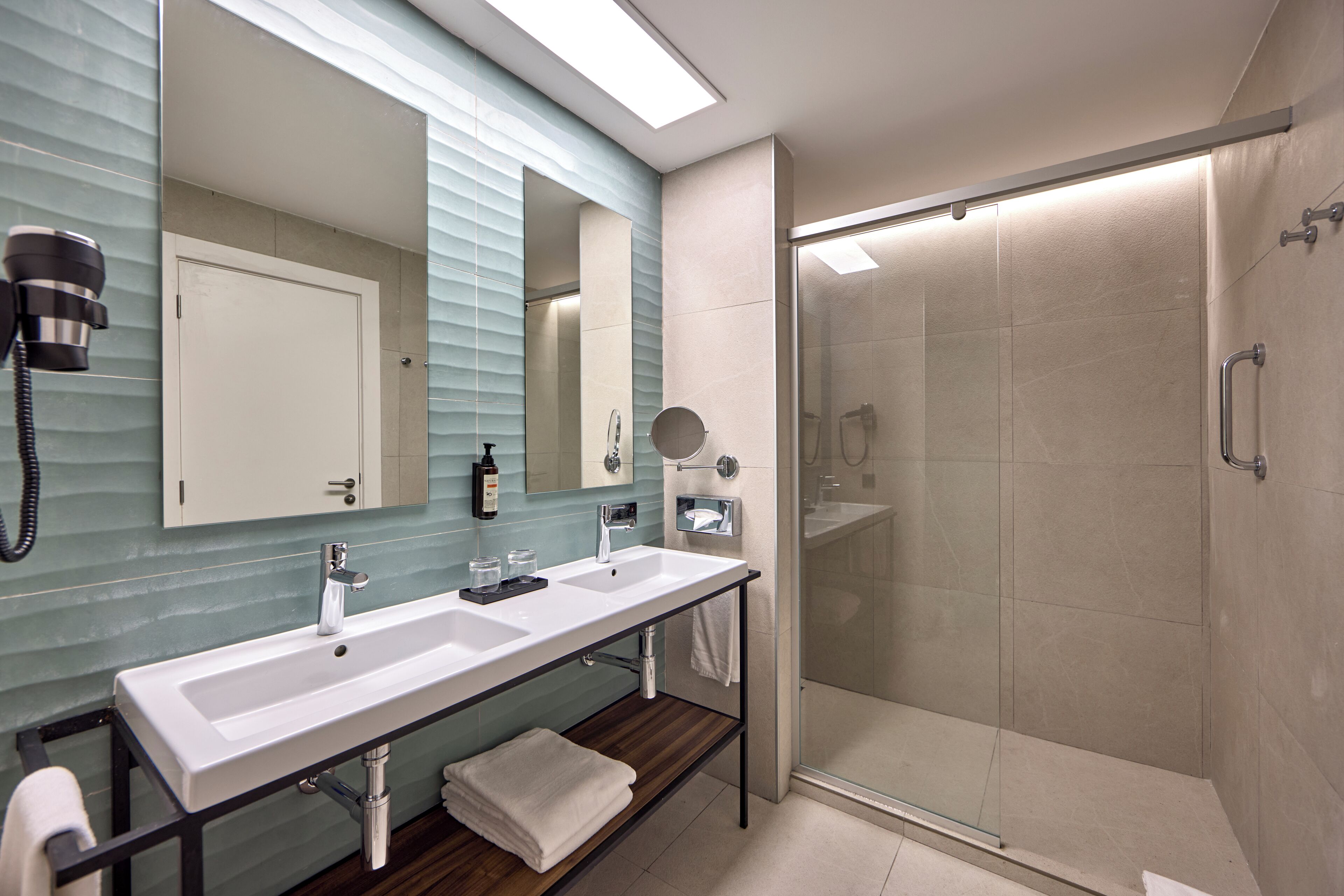 Een moderne badkamer met twee wastafels, een spiegel en een douche met glazen wanden.