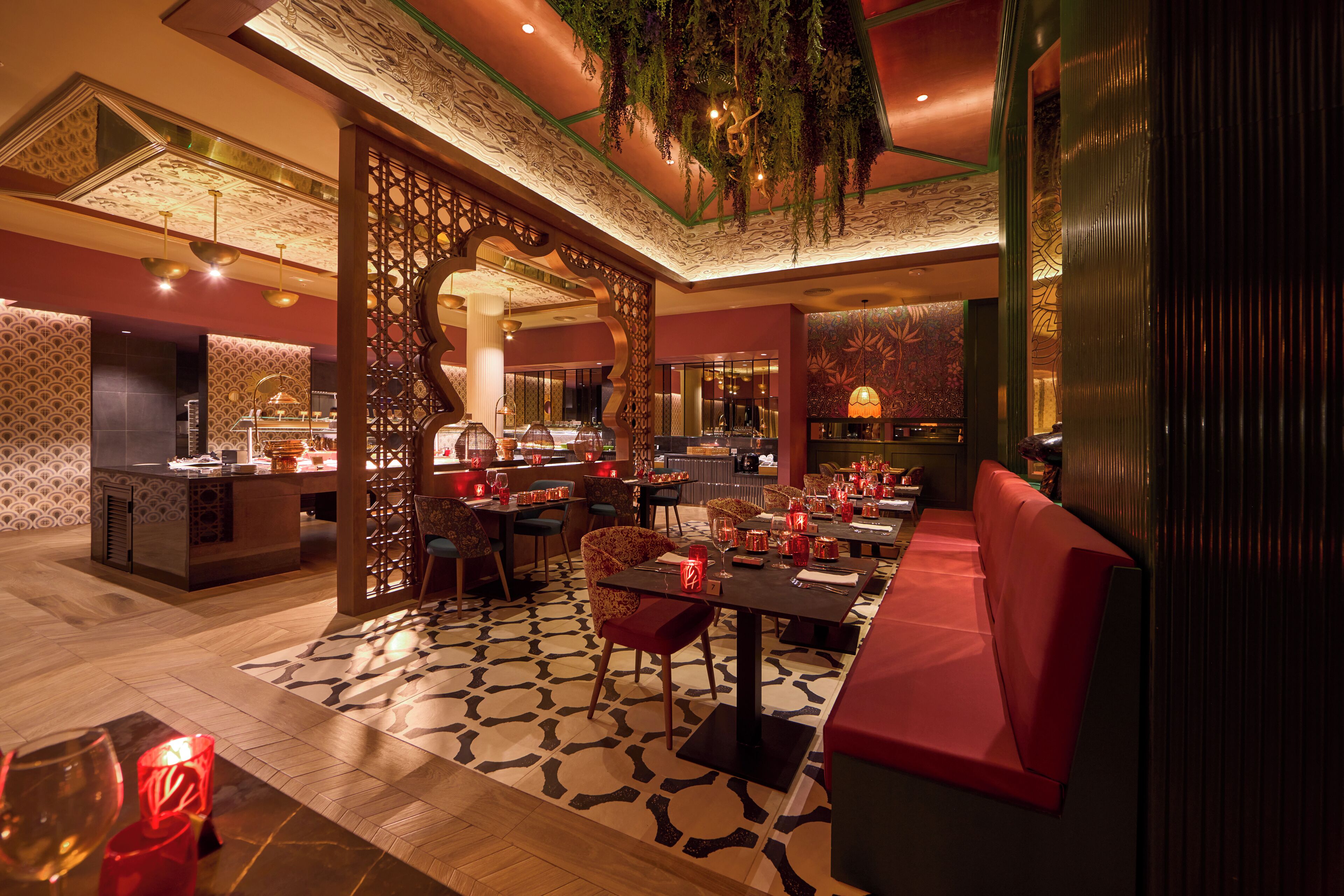 A restaurant with a patterned floor, red seating, and hanging plants.