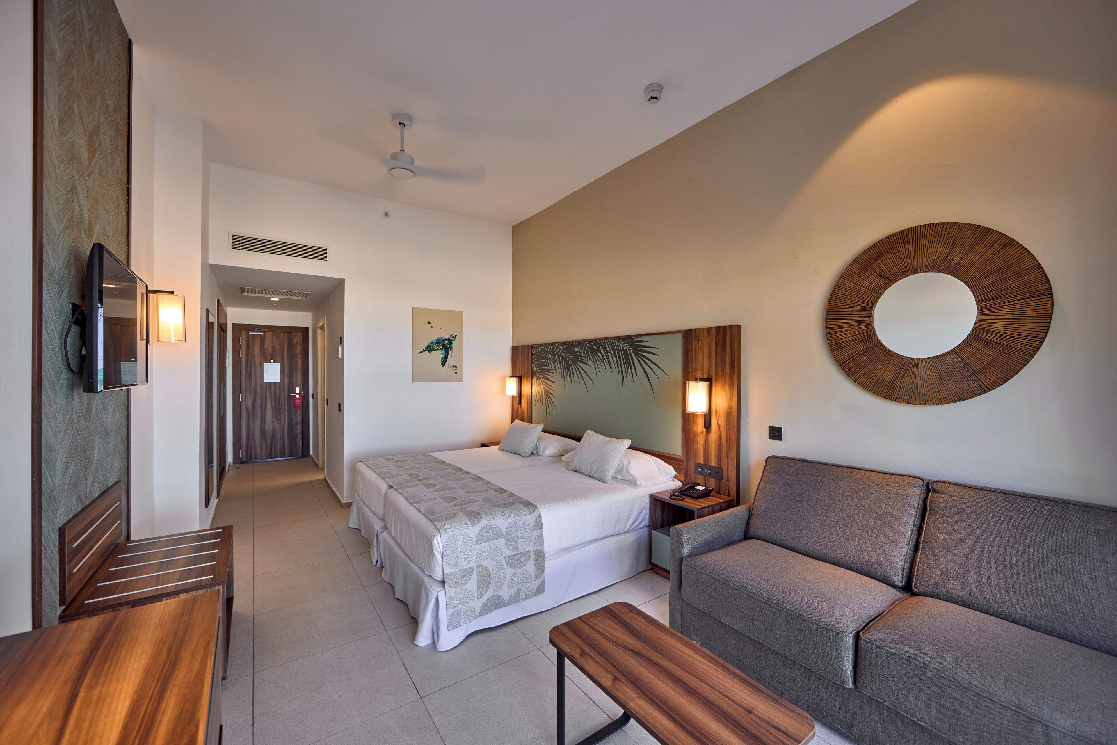 Une chambre d’hôtel avec un lit, un canapé, une télévision, un bureau et un miroir.