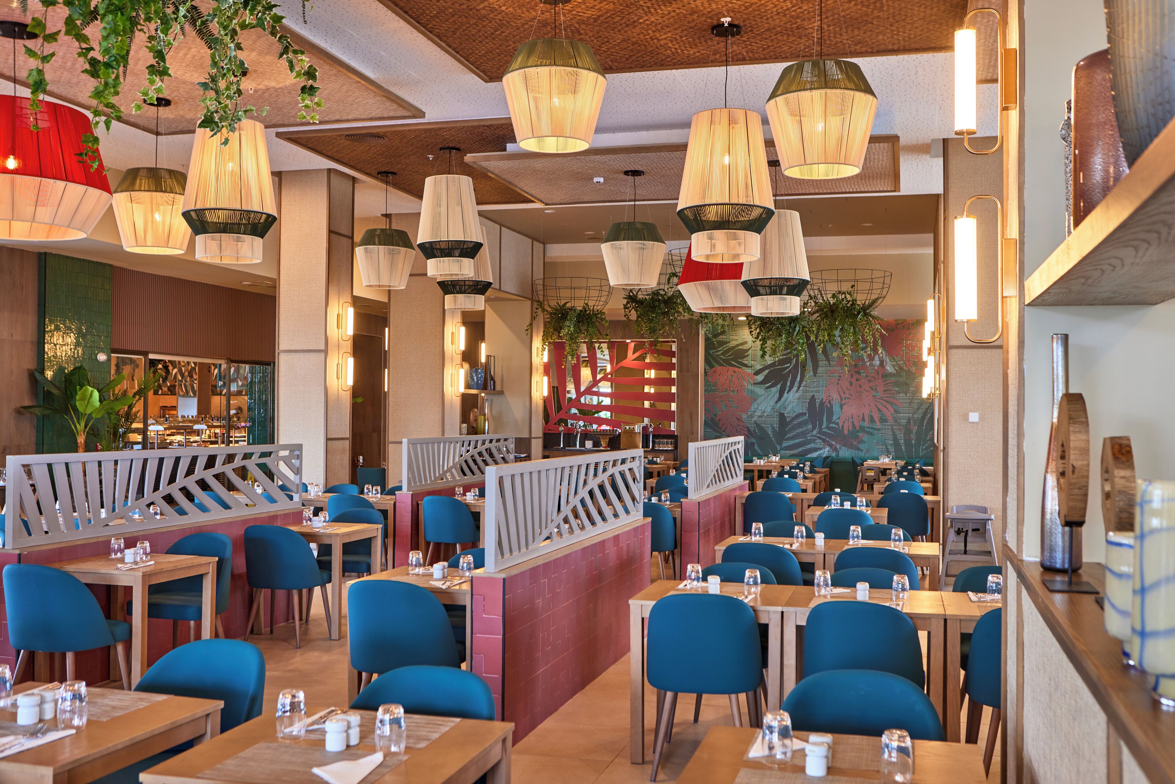 A restaurant with multiple tables and chairs, hanging pendant lights, and a decorative wall mural.