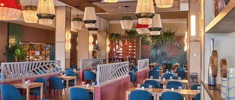 A restaurant with multiple tables and chairs, hanging pendant lights, and a decorative wall mural.