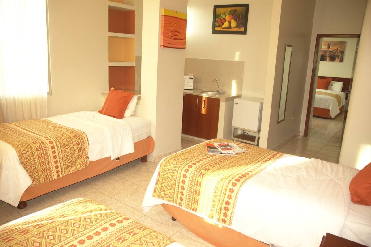 Une chambre d’hôtel avec deux lits, une petite kitchenette et un miroir qui reflète la pièce.