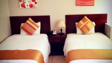 Habitación de hotel con dos camas, cada una con cabecero, mesita de noche y lámpara.