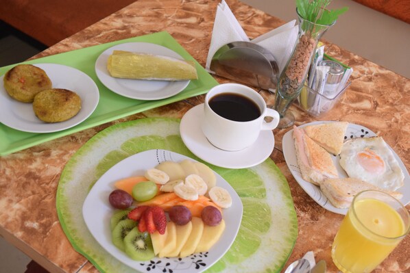 Une table de petit-déjeuner avec des assiettes de fruits, une tasse de café, un verre de jus de fruits et un sandwich.