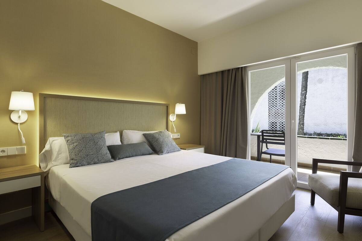 Une chambre d’hôtel avec un grand lit, deux tables de chevet, une chaise et un balcon avec vue.
