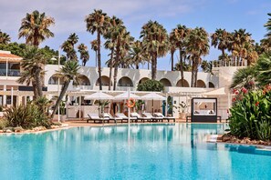 A pool area with lounge chairs, umbrellas, and palm trees. - AluaSoul Menorca Hotel - Adults Only (Sant Lluis)