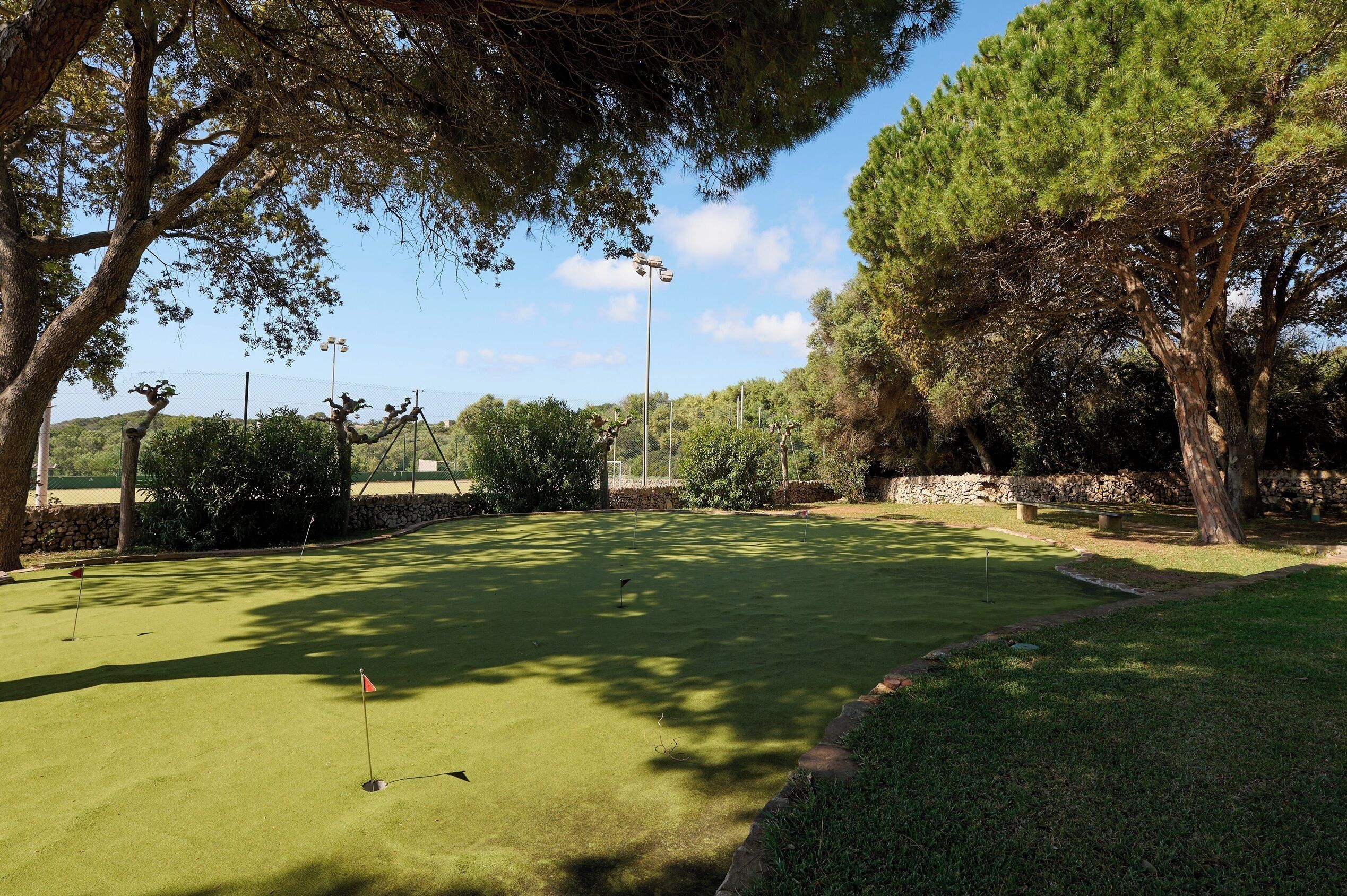 A golf course with a well-maintained green, trees, and a stone wall in the background.