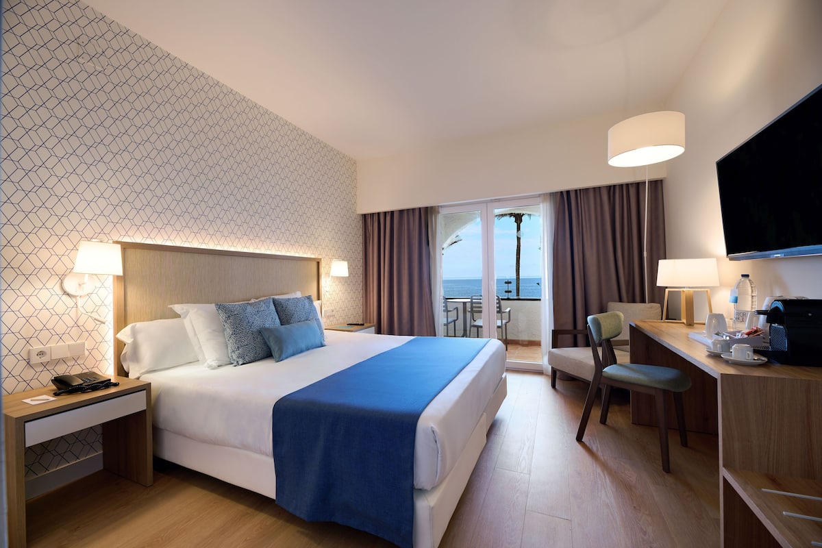 Une chambre d’hôtel équipée d’un lit, d’un bureau et d’une chaise, d’une télévision et offrant une vue sur l’océan.