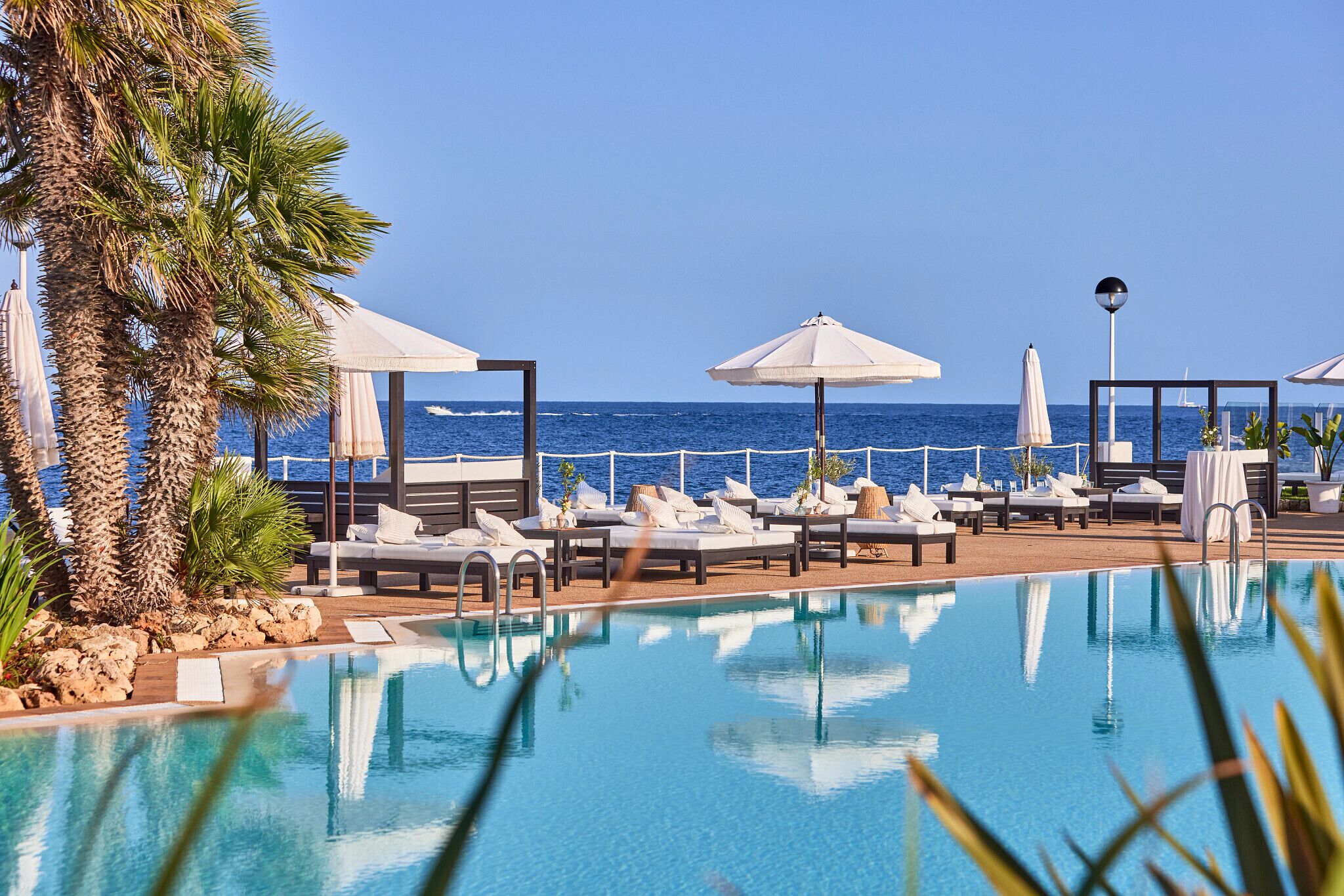 A poolside area with lounge chairs and umbrellas, overlooking the sea.