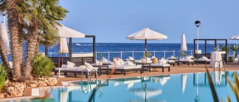 A poolside area with lounge chairs and umbrellas, overlooking the sea.