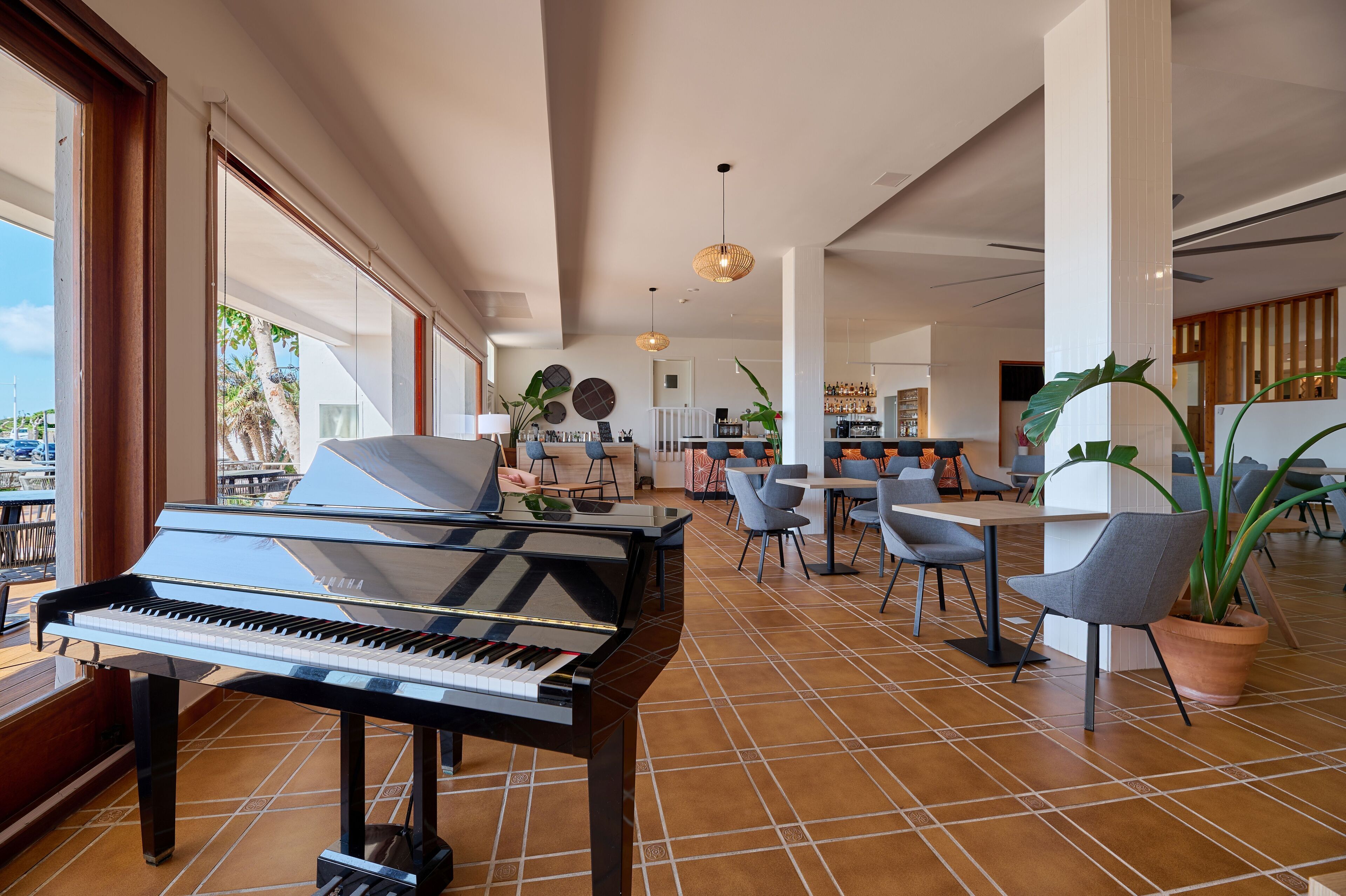 A spacious hotel lobby with a grand piano, modern furniture, and large windows offering a view of the outdoors.