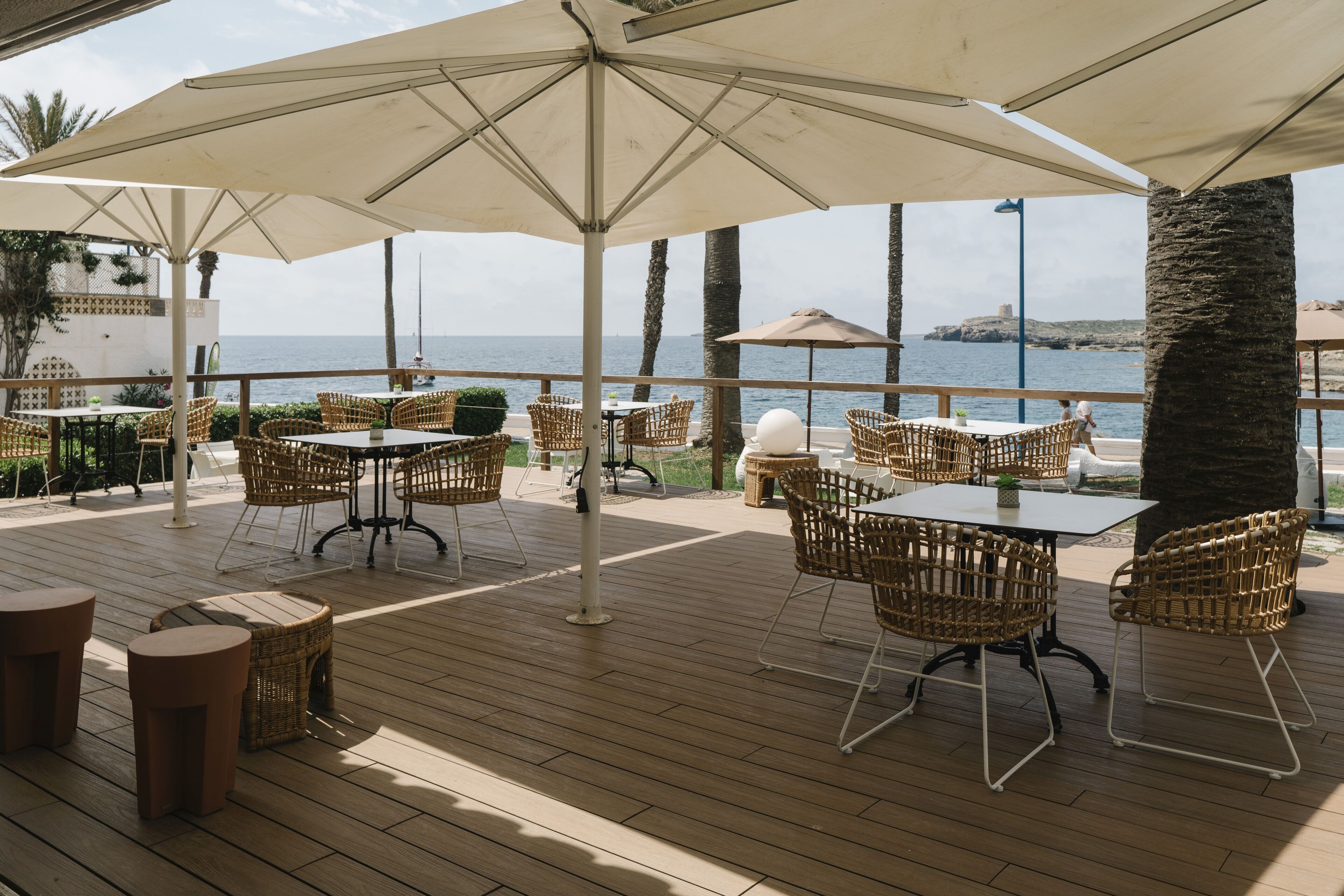 An outdoor patio with wicker furniture and umbrellas, overlooking the sea.
