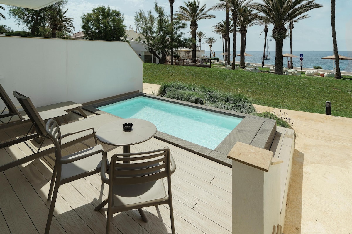 Un espace piscine agrémenté d’une table et de chaises, entouré d’un mur blanc et de palmiers.