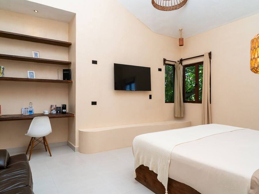 A bedroom with a bed, a desk, a chair, and a television on the wall.