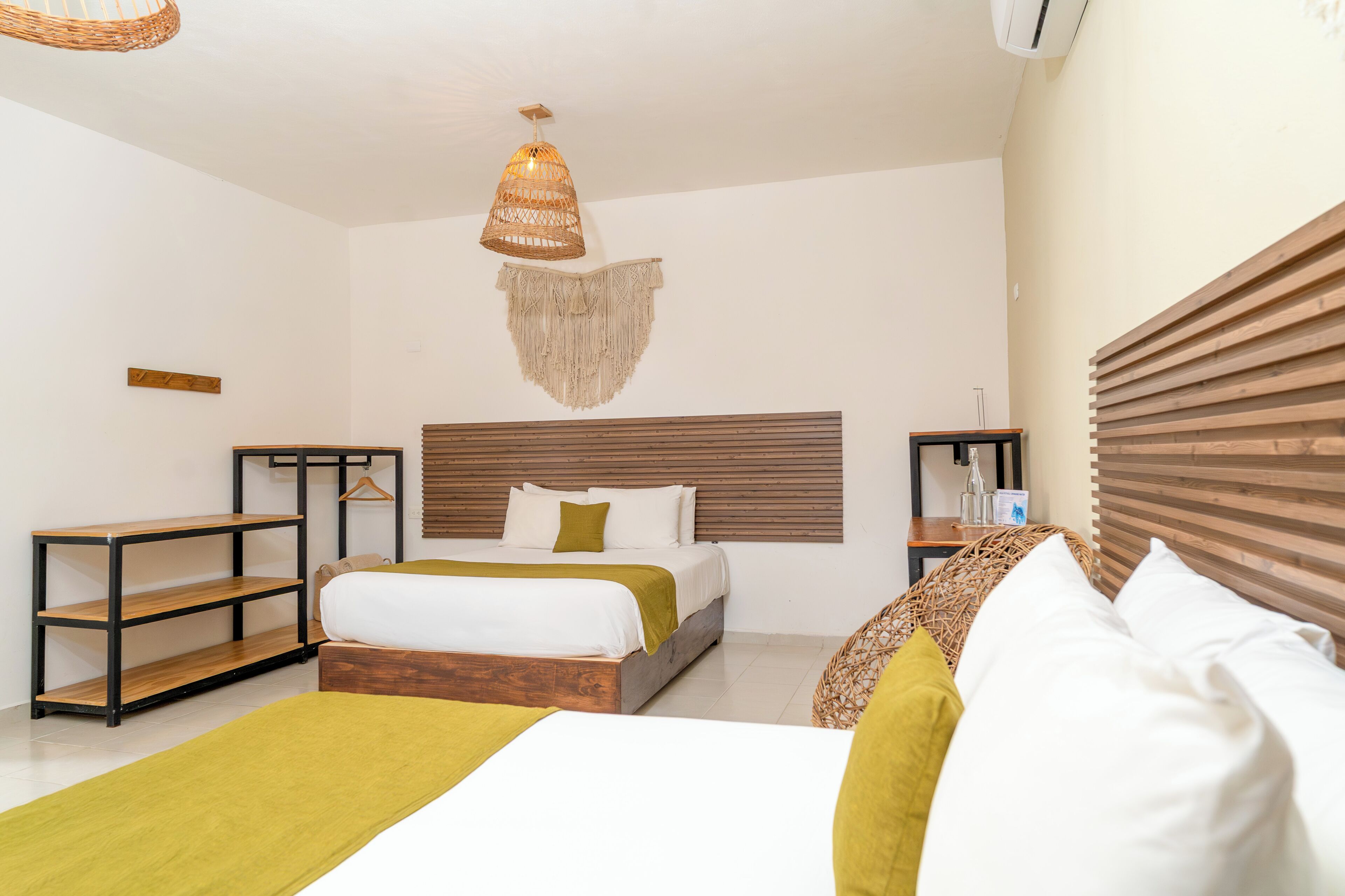 A hotel room with a bed, a hanging light fixture, a wooden headboard, a small table, and a shelf.