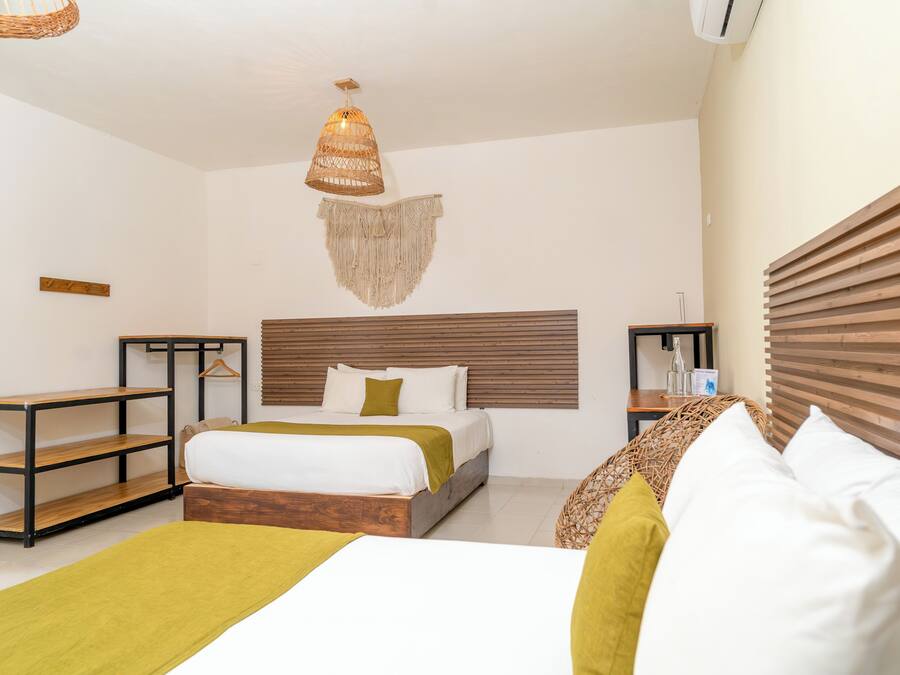 A hotel room with a bed, a hanging light fixture, a wooden headboard, a small table, and a shelf.