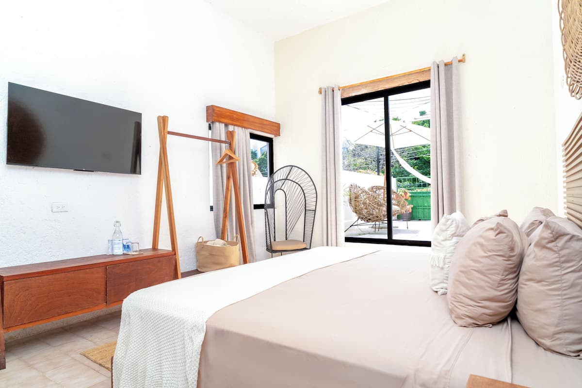 A bedroom with a bed, a TV, a wooden dresser, a chair, and a window with curtains.