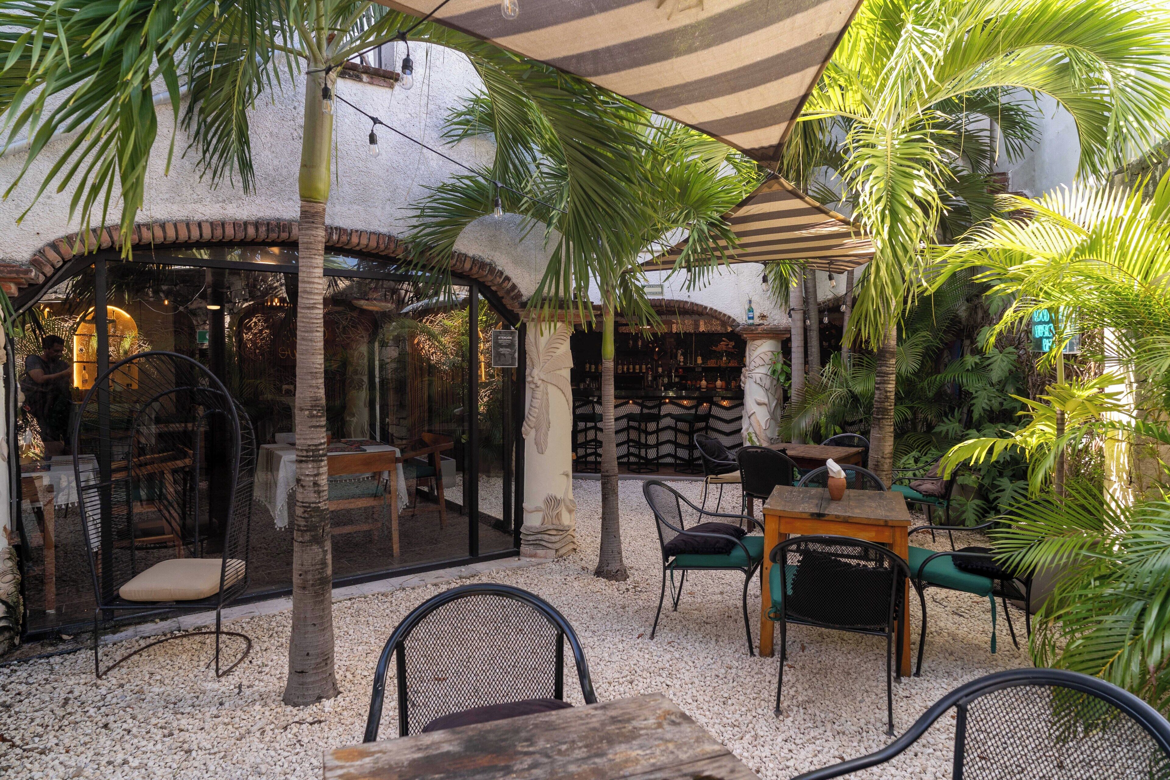 An outdoor seating area with tables and chairs, palm trees, and a bar.