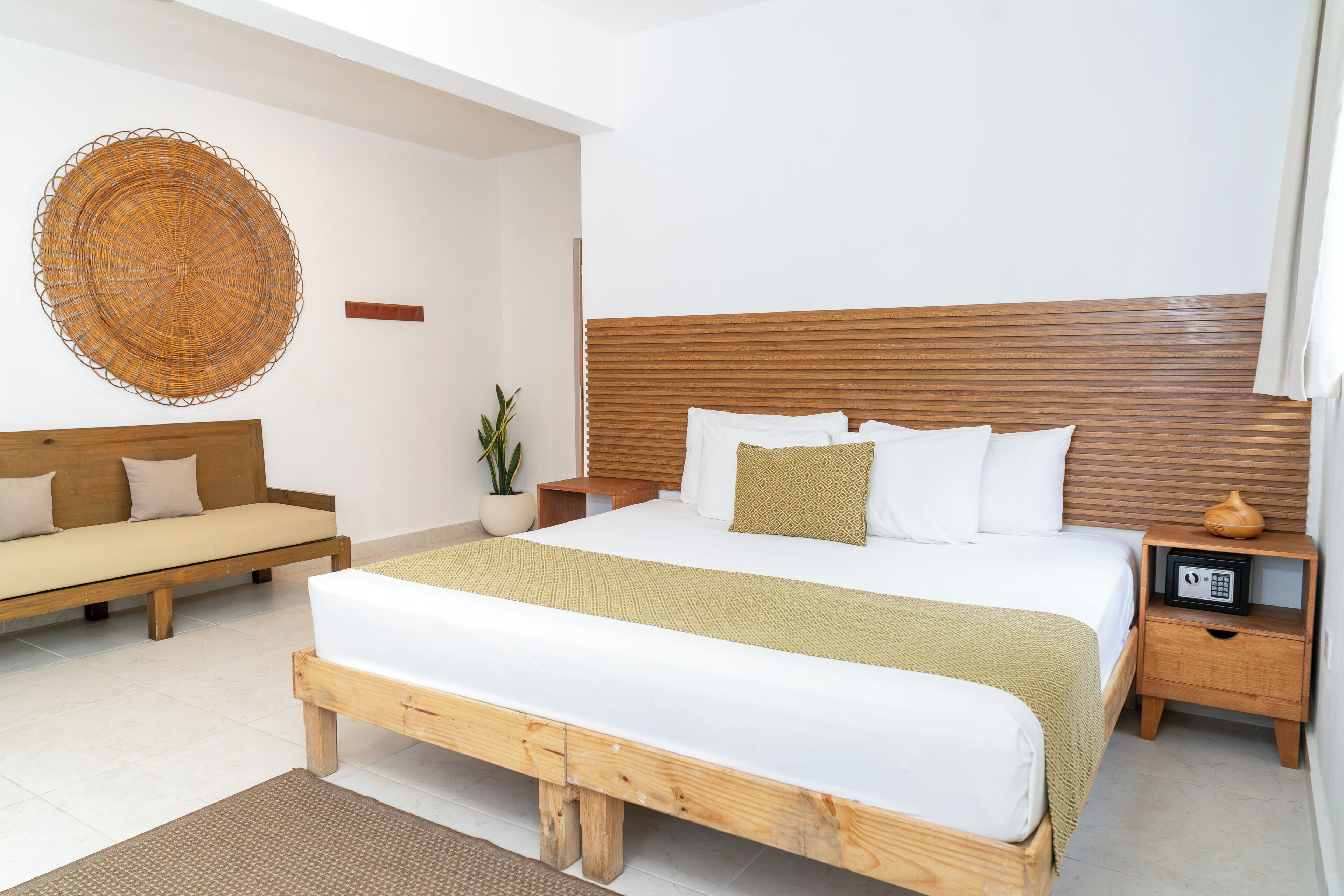 A modern bedroom with a wooden bed, a bench, a bedside table with a lamp, and a wall-mounted decorative item.