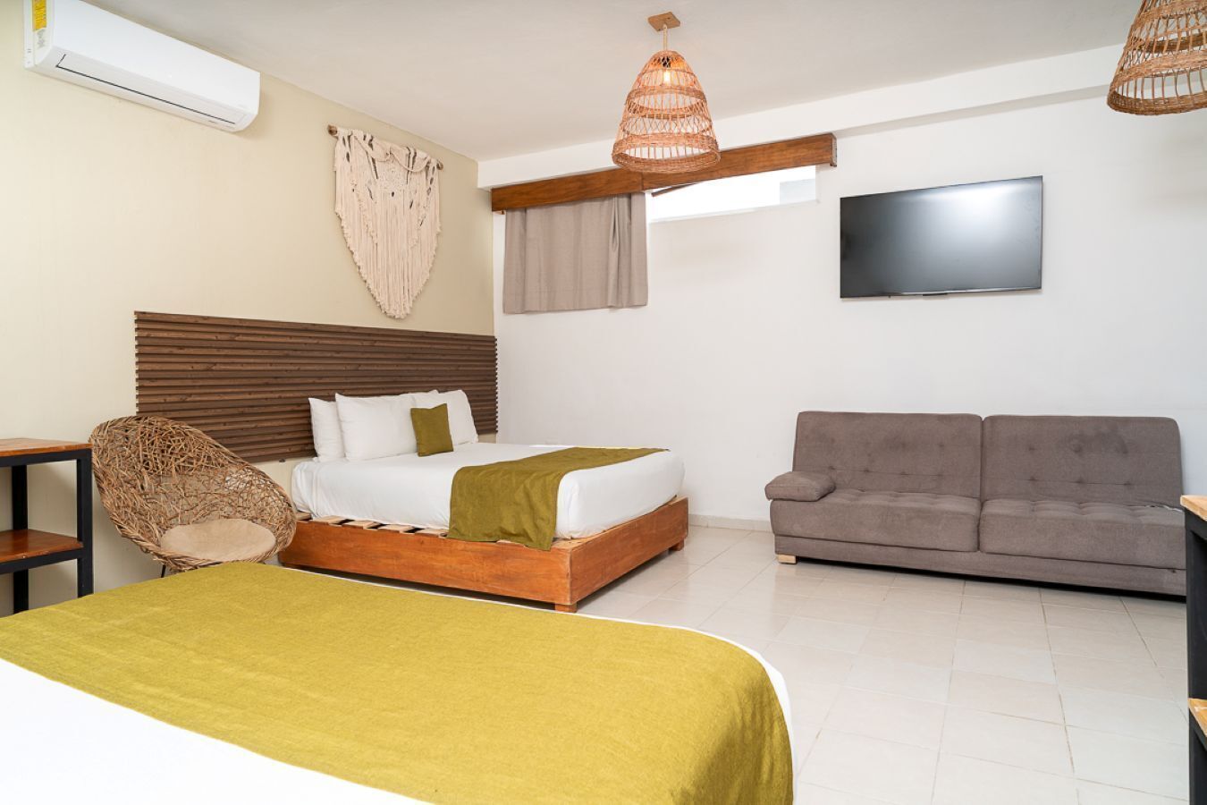 A hotel room with a bed, a sofa, a television, and a hanging light fixture.