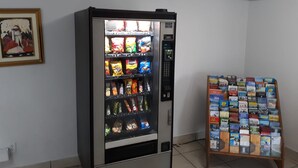 A vending machine with snacks and beverages, a small display of cigarette packs, and a framed picture on the wall. - OYO Hotel Pensacola I-10 & Hwy 29 (Pensacola)