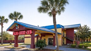 A Palm Court Inn with a red and yellow facade, a covered entrance, and a parking lot. - OYO Hotel Pensacola I-10 & Hwy 29 (Pensacola)