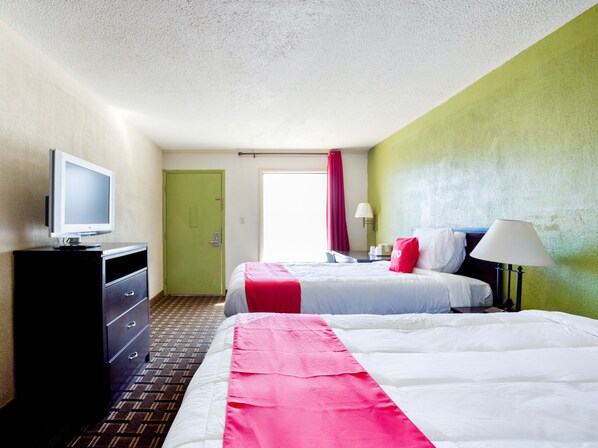 A hotel room with two beds, a television on a dresser, and a green wall.