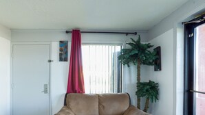 A living room with a beige sofa, a red curtain, a potted plant, and a door. - OYO Hotel Pensacola I-10 & Hwy 29 (Pensacola)