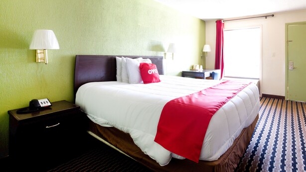 A hotel room with a bed, bedside tables, lamps, a telephone, and a window with curtains. - OYO Hotel Pensacola I-10 & Hwy 29 (Pensacola)