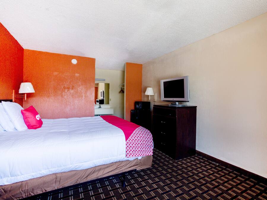 Habitación de hotel con cama, televisor, cómoda y espejo.