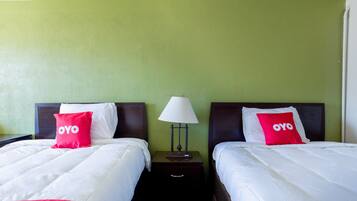 A hotel room with two beds, each with a white and red bedspread, and a lamp between them.