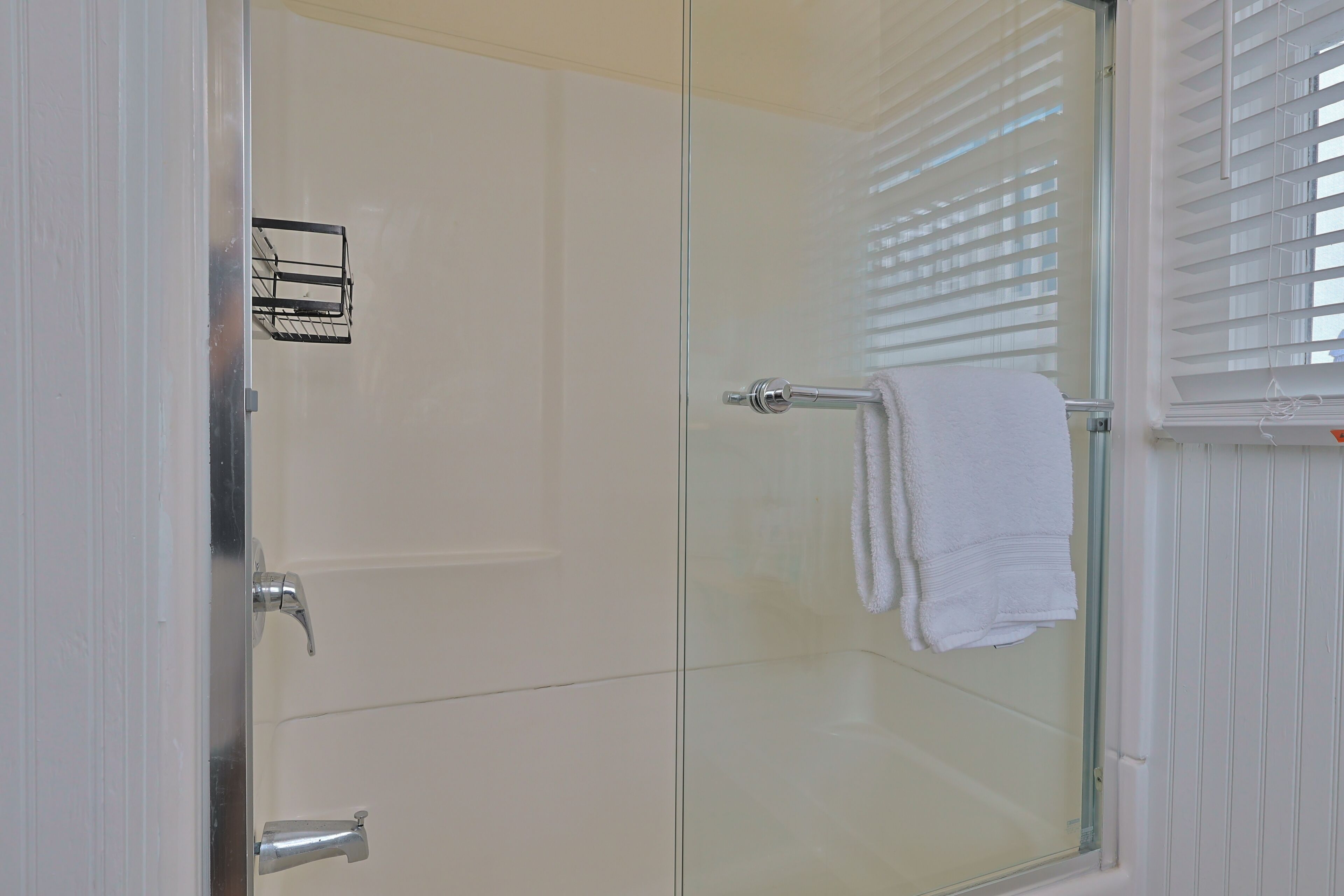 Une douche fermée par des parois de verre, avec une serviette blanche accrochée à la poignée de la porte.