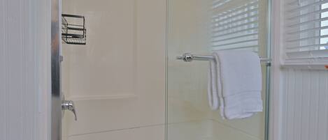 Une douche fermée par des parois de verre, avec une serviette blanche accrochée à la poignée de la porte.