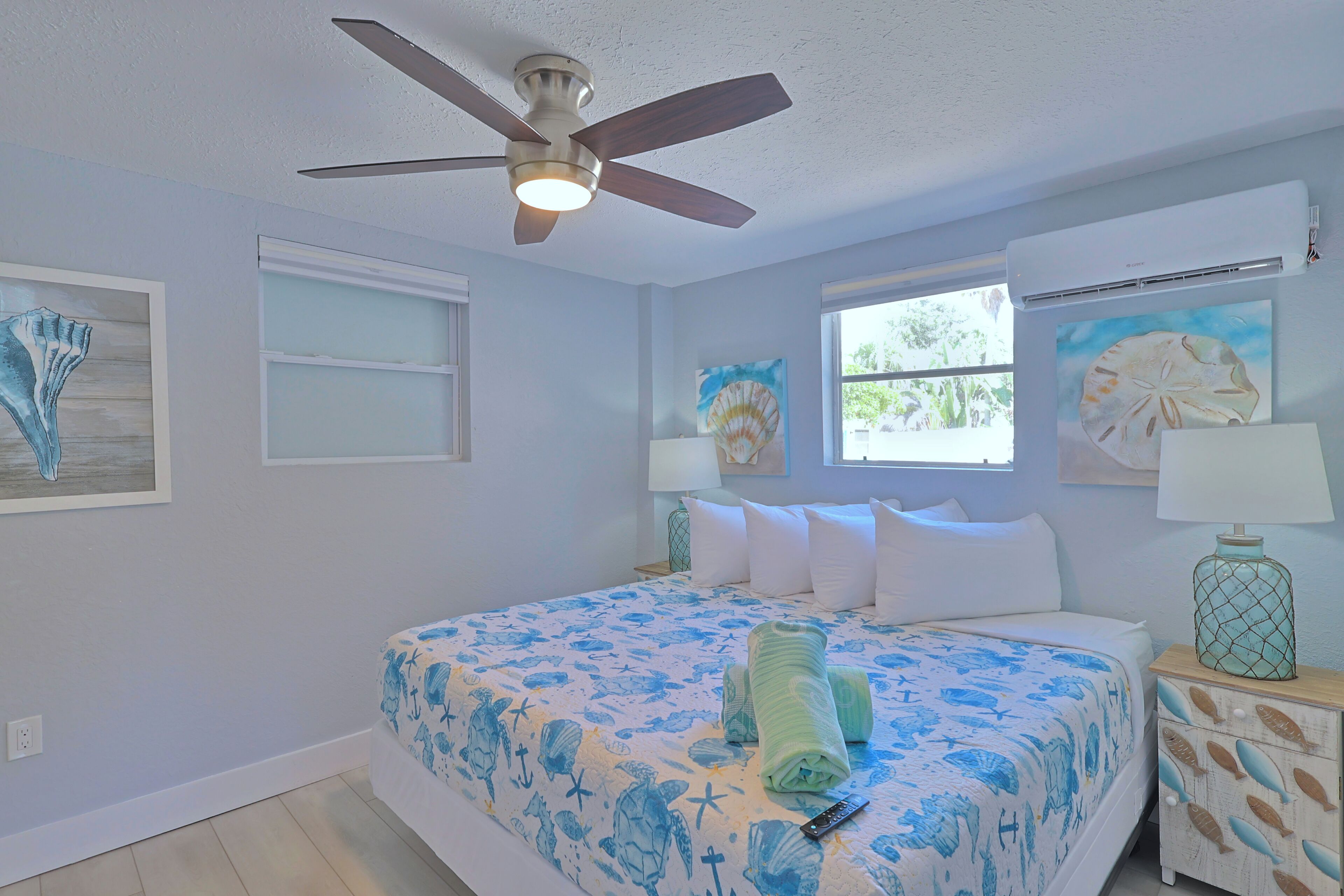 A bedroom with a bed, ceiling fan, artwork, and a window.