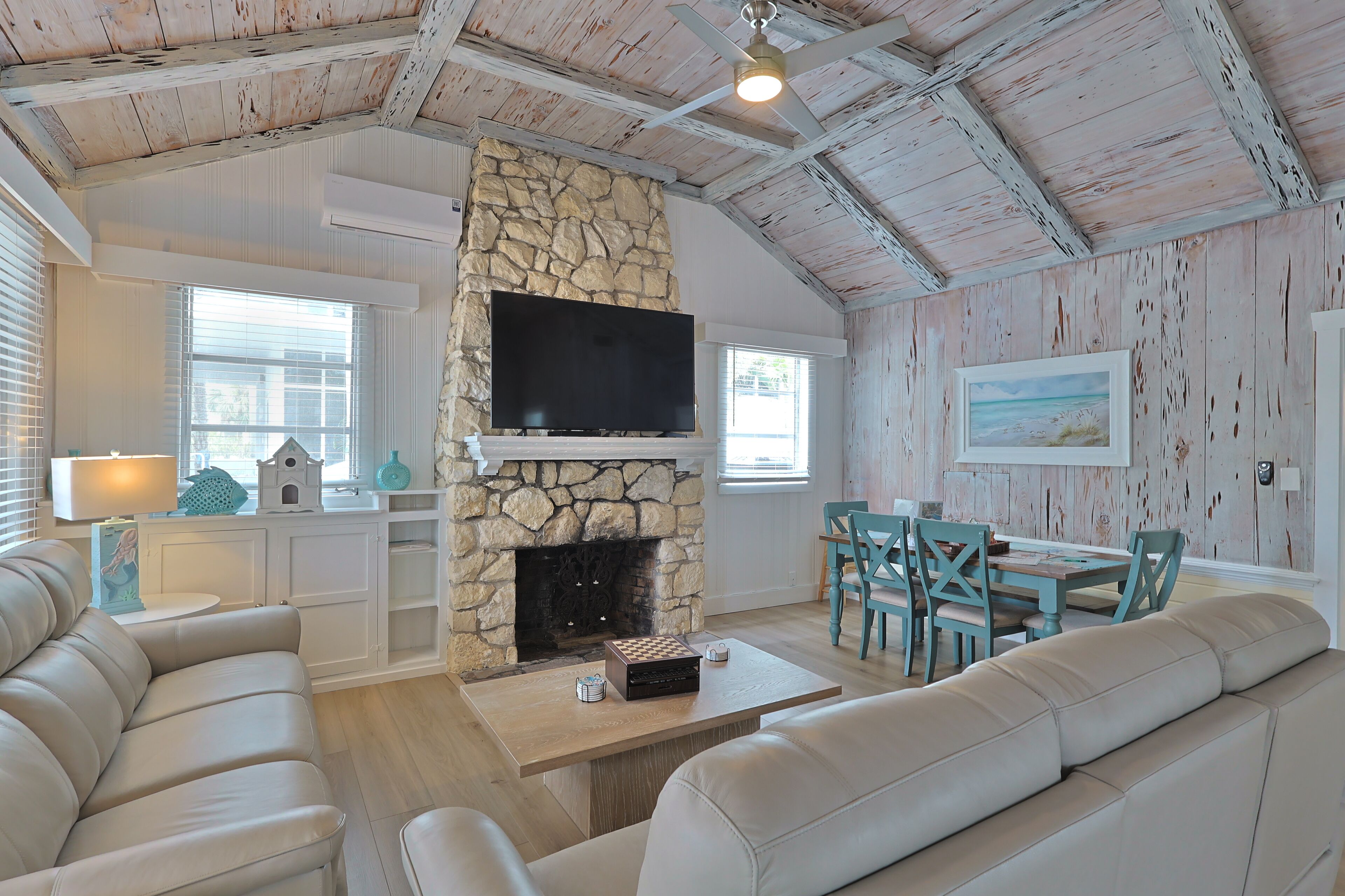 A living room with a stone fireplace, a flat-screen TV, a sofa, and a dining area with chairs.
