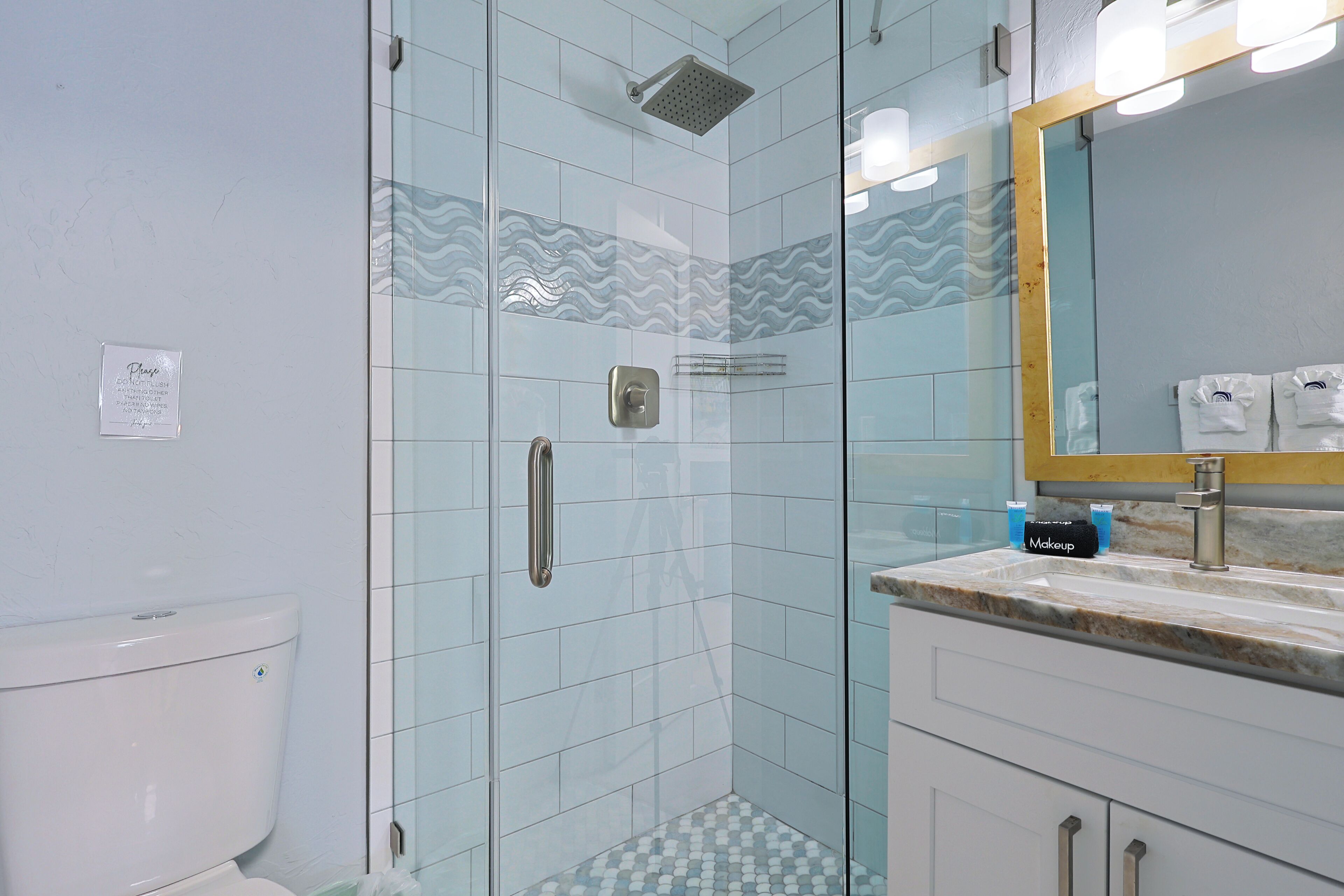 A bathroom with a glass-enclosed shower, a sink with a marble countertop, and a mirror with a gold frame.