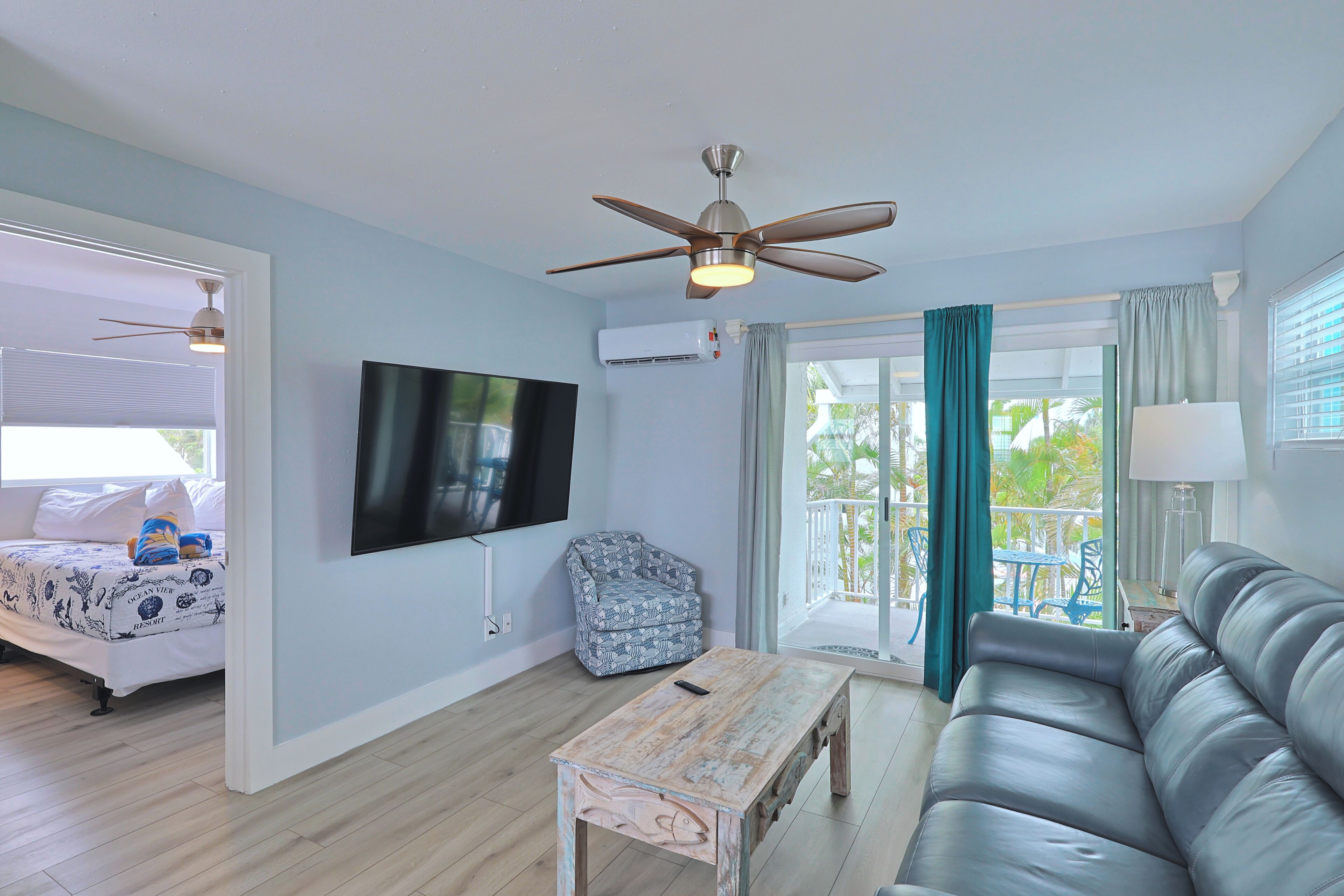 A living room with a flat-screen TV, a ceiling fan, a sofa, a coffee table, and a chair.
