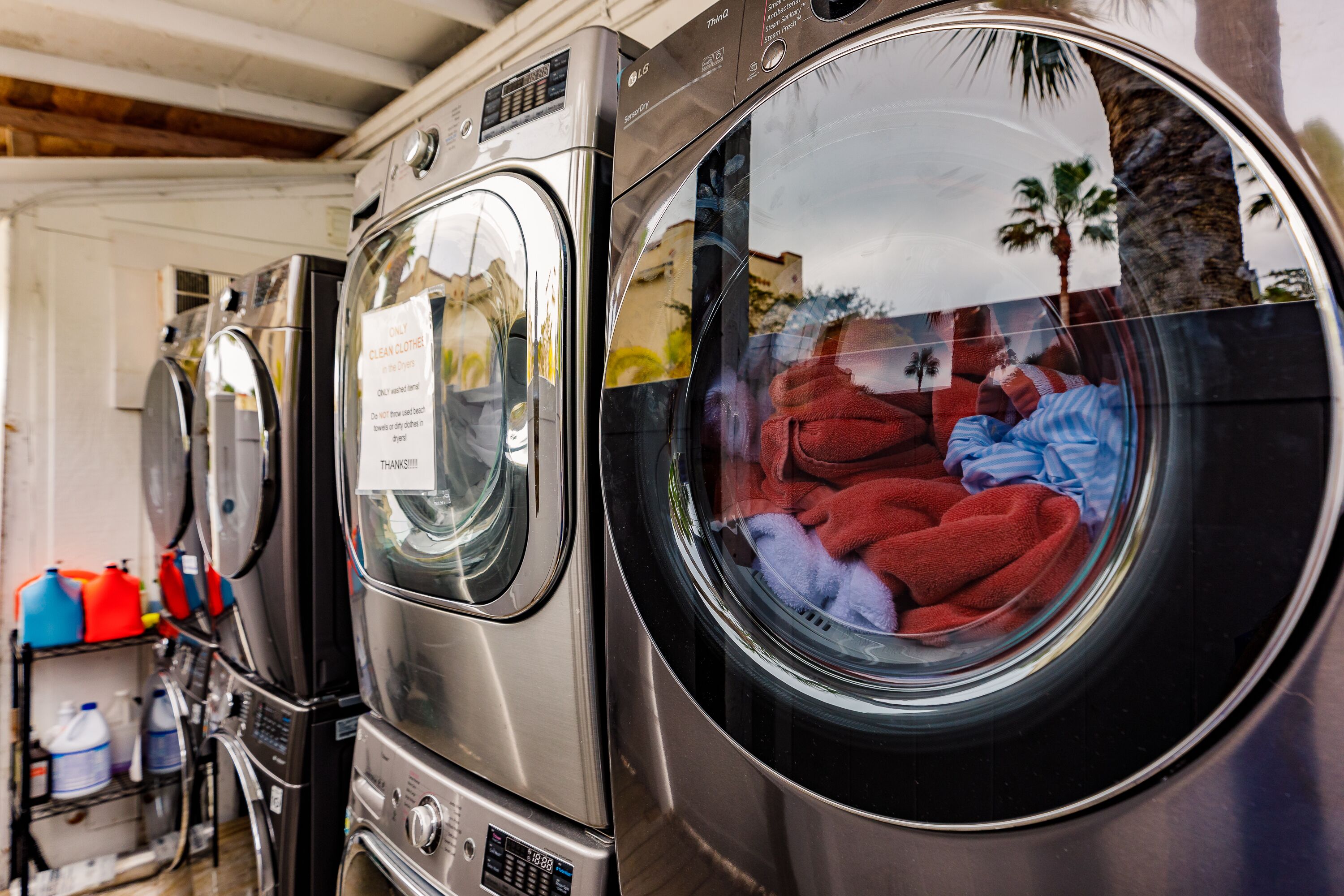 A row of stainless steel front-loading washers with a sign on one stating "ONLY CLEAN CLOTHES".