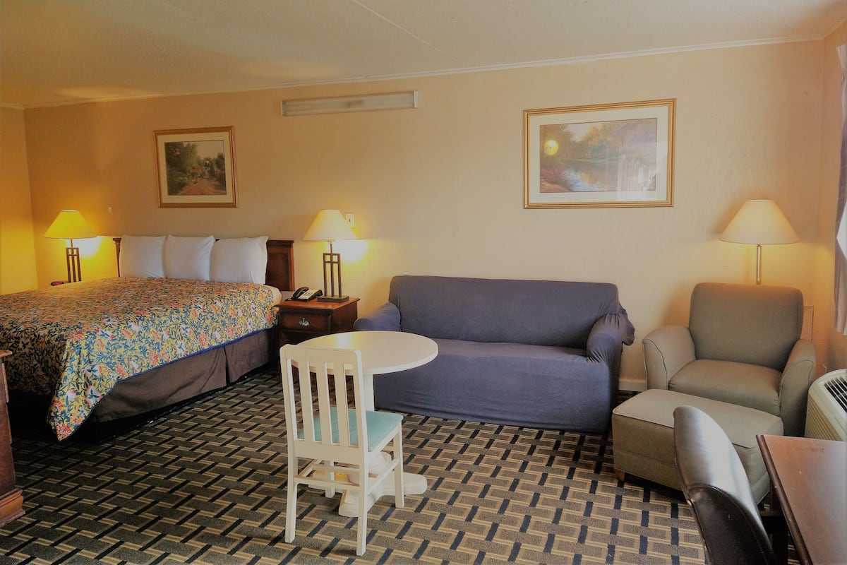 Une chambre d’hôtel comprenant un lit, un canapé, une chaise, une petite table et deux lampes.