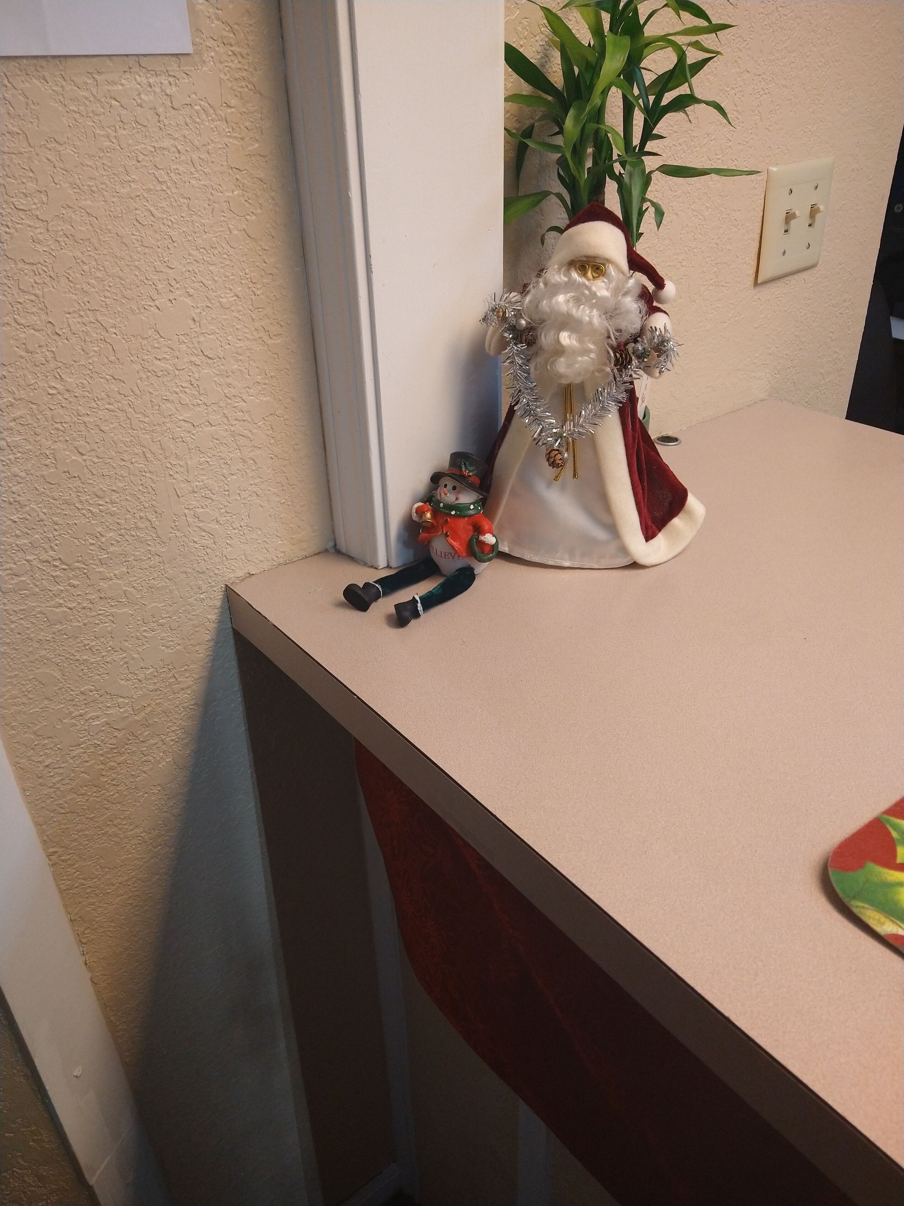 Una encimera de cocina con una figura decorativa de un muñeco de nieve, una planta pequeña y un objeto rojo y verde.
